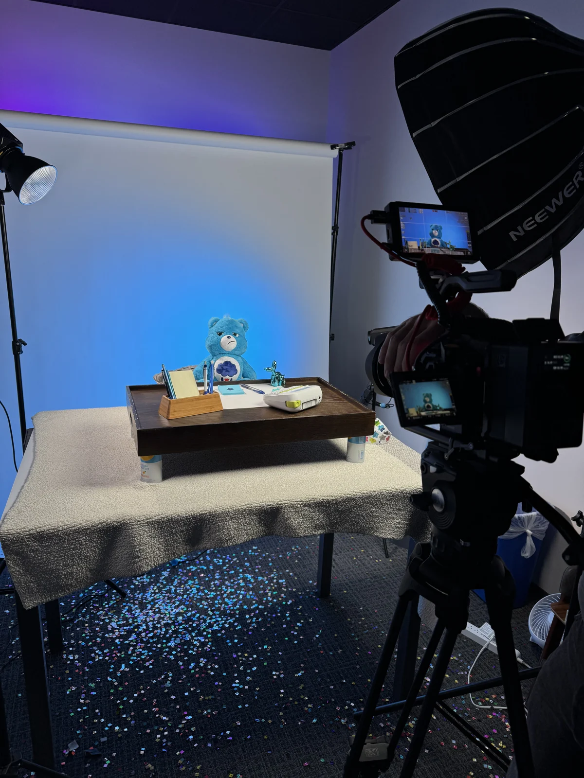 Camera and softbox pointed at a bear on a styled table with confetti on the floor